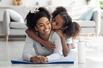 Happy black mother and daughter cuddling while practicing yoga
