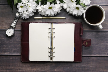 An open notebook near a bouquet of chrysanthemums. Cup of coffee wrist watch on a wooden background.