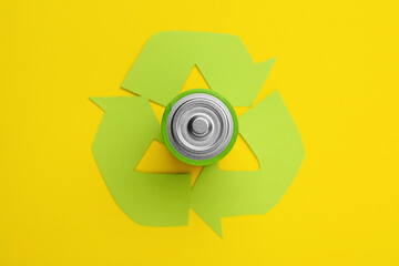 Used battery and recycling symbol on yellow background, top view