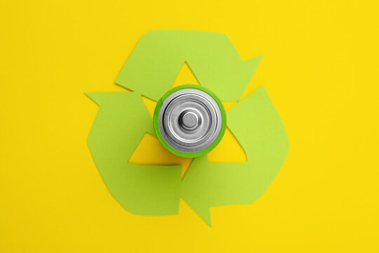 Used battery and recycling symbol on yellow background, top view