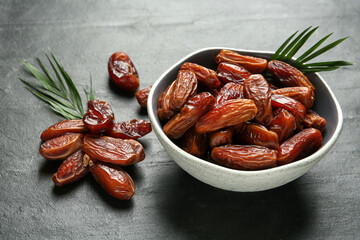 Tasty sweet dried dates and green leaves on black table