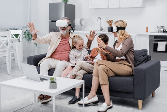 children using digital tablet near excited grandparents gaming in vr headsets.