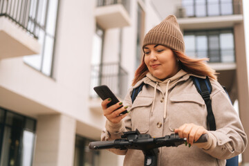Close-up portrait of woman wearing warm hat and jacket using mobile phone to unlock electric...