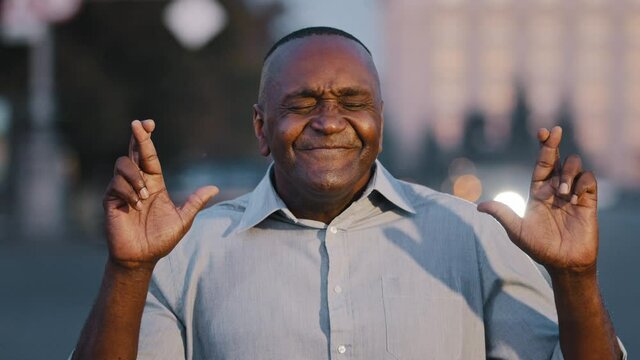 Hopeful elderly American male entrepreneur believer cross fingers make wish outdoors, man senior businessman desperate superstitious person make gesture hope believe in good luck