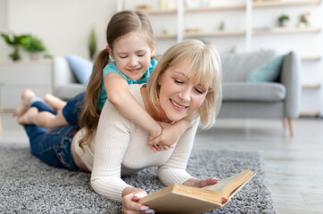 Happy mature woman and granddaughter reading book