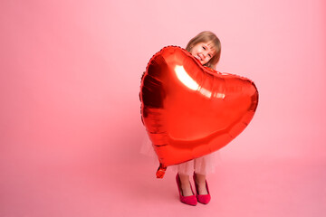 Obraz na płótnie Canvas Beautiful child girl with big red heart balloon on pink background celebrating Valentine day
