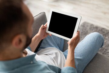 Unrecognizable young guy working on tablet computer with empty screen at home office, mockup for website or app