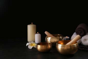 Composition with golden singing bowls on black table against dark background, space for text