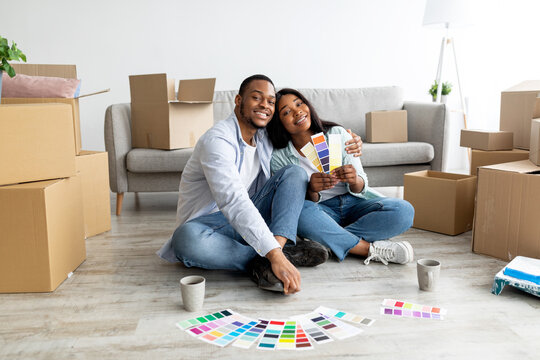 Happy african american couple planning renovation and dreaming, choosing color palettes together, sitting in new house