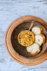 Bread baguette with homemade hummus in an old clay plate on a wooden table. A plant-based, healthy, vitamin-rich, balanced vegan food. Dish with red onion, pepper, dill and olive oil. Middle East.