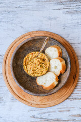 Bread baguette with homemade hummus in an old clay plate on a wooden table. A plant-based, healthy, vitamin-rich, balanced vegan food. Dish with red onion, pepper, dill and olive oil. Middle East.