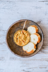 Bread baguette with homemade hummus in an old clay plate on a wooden table. A plant-based, healthy, vitamin-rich, balanced vegan food. Dish with red onion, pepper, dill and olive oil. Middle East.