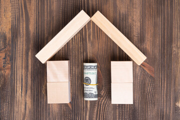 The concept of selling and buying real estate. Paper dollar bills rolled up inside a wooden house made of blocks, top view