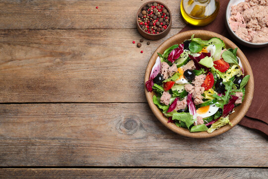 Bowl of delicious salad with canned tuna and vegetables on wooden table, flat lay. Space for text