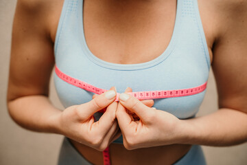 Cropped view of slim woman measuring breasts with tape measure at home, close up. Unrecognizable...