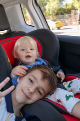 small blond baby infant in car seat hugs his big brother