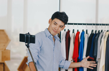 Fototapeta premium Young Asian man blogger is broadcasting a video for selling clothes online, focus on camera.