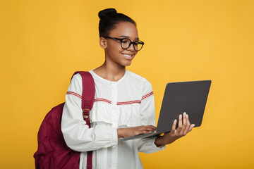 Smiling smart pretty teenage black girl pupil in glasses with backpack studying with laptop, prepare to exam