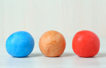 Different color play dough balls on white wooden table, closeup