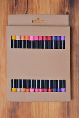 Set of sketching markers in a beautiful cardboard box packaging on a wooden texture background. Top view, close-up