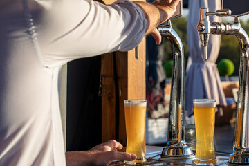 bartender hand on cold beer tap pouring a draft beer outdoors on a summer day