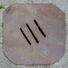 Grungy makeshift sewer manhole - crooked cut rusty textured metal plate with a slotted grate 