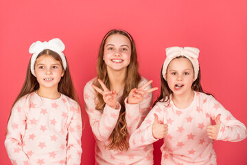 Giving double thumbs and v-signs. Happy girls in homewear pink background. Children homewear