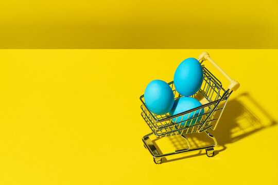 A shopping cart with colourful blue eggs on a yellow background