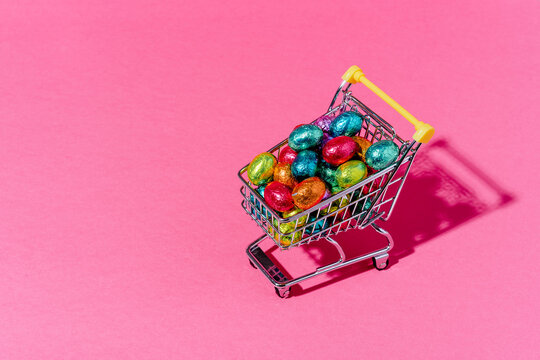A shopping cart with colourful chocolate eggs on a pink background.