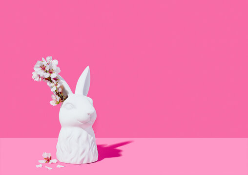 Bust of a white rabbit with almond blossoms on a pink background