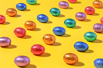 Pattern of colourful chocolate foil eggs on a yellow background