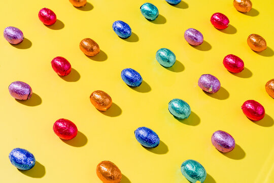 Pattern of colourful chocolate foil eggs on a yellow background
