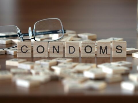 condoms concept represented by wooden letter tiles on a wooden table with glasses and a book