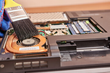 The wizard cleans the laptop's cooling system with a brush and a vacuum cleaner. PC care and repair concept.