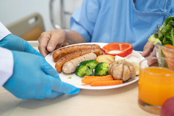 Asian senior or elderly old lady woman patient eating breakfast and vegetable healthy food with hope and happy while sitting and hungry on bed in hospital.