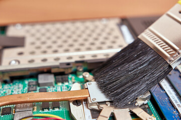 Fototapeta premium The wizard cleans the laptop's cooling system with a brush and a vacuum cleaner. PC care and repair concept.