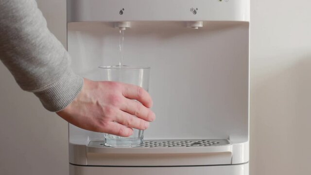The man takes a glass of water from the water dispenser. Clean water for healty life.