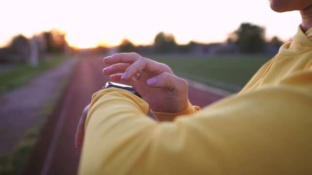 Fit woman use smart watch at sunset. Runner checking pulse on smartwatch on running workout. Modern technology and a healthy lifestyle. Athlete run woman check pulse on fitness bracelet.