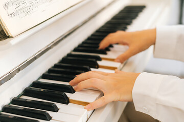 Fototapeta premium Close-up hands of unrecognizable musician female pianist playing gentle music on white classical piano in light classroom. Closeup view of woman music composer practicing piano at home studio.