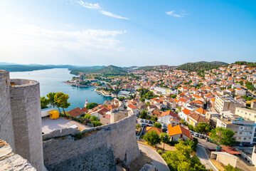 Coastal view of Sibenik old city, Croatia. Cathedral of St James, adriatic sea with island in background. Summer weather, aerial view of city roofs. UNESCO heritage. - obrazy, fototapety, plakaty