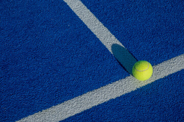 Racket sports. Paddle tennis ball next to the line of a blue paddle tennis court.