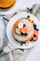 Tasty pancakes with strawberry, blueberry and banana in a white plate on the table. top view