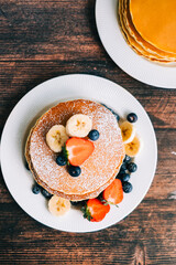 Tasty pancakes with strawberry, blueberry and banana in a white plate on the table. top view