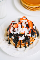 Tasty pancakes with strawberry, coconut chips and hot chocolate in a white plate on the table.