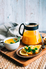 Brewed sea buckthorn tea in a teapot with orange in glass cups with fresh orange, mint and honey.