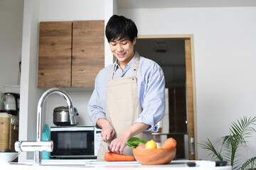 キッチンで料理をするエプロン姿の若い黒髪の男性