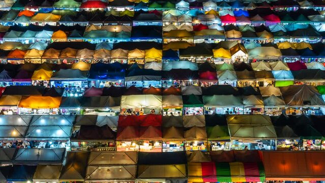 Zoom out time lapse view of colourful food stalls at the popular Ratchada Night Market in Bangkok, Thailand. 