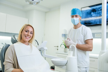 Middle shot of a happy Caucasian woman with a bright smile sitting in the dental chair and her male dentist, before a teeth exam.