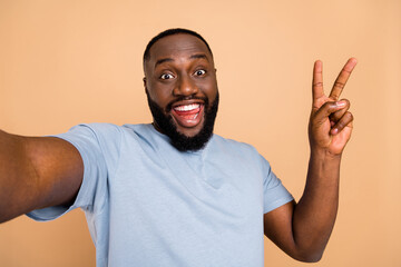 Self-portrait of attractive cheerful childish guy showing v-sign good mood isolated over beige...