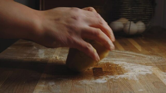 Hands knead a pasta dough or baking dough on a rustic kitchen table